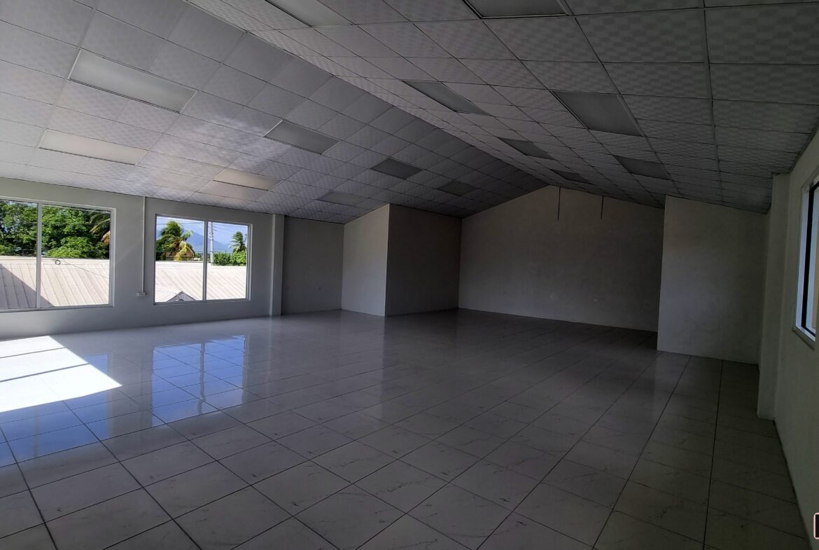 A large, empty room with expansive windows along one wall. Sunlight streams through the windows, illuminating the dust particles floating in the air.