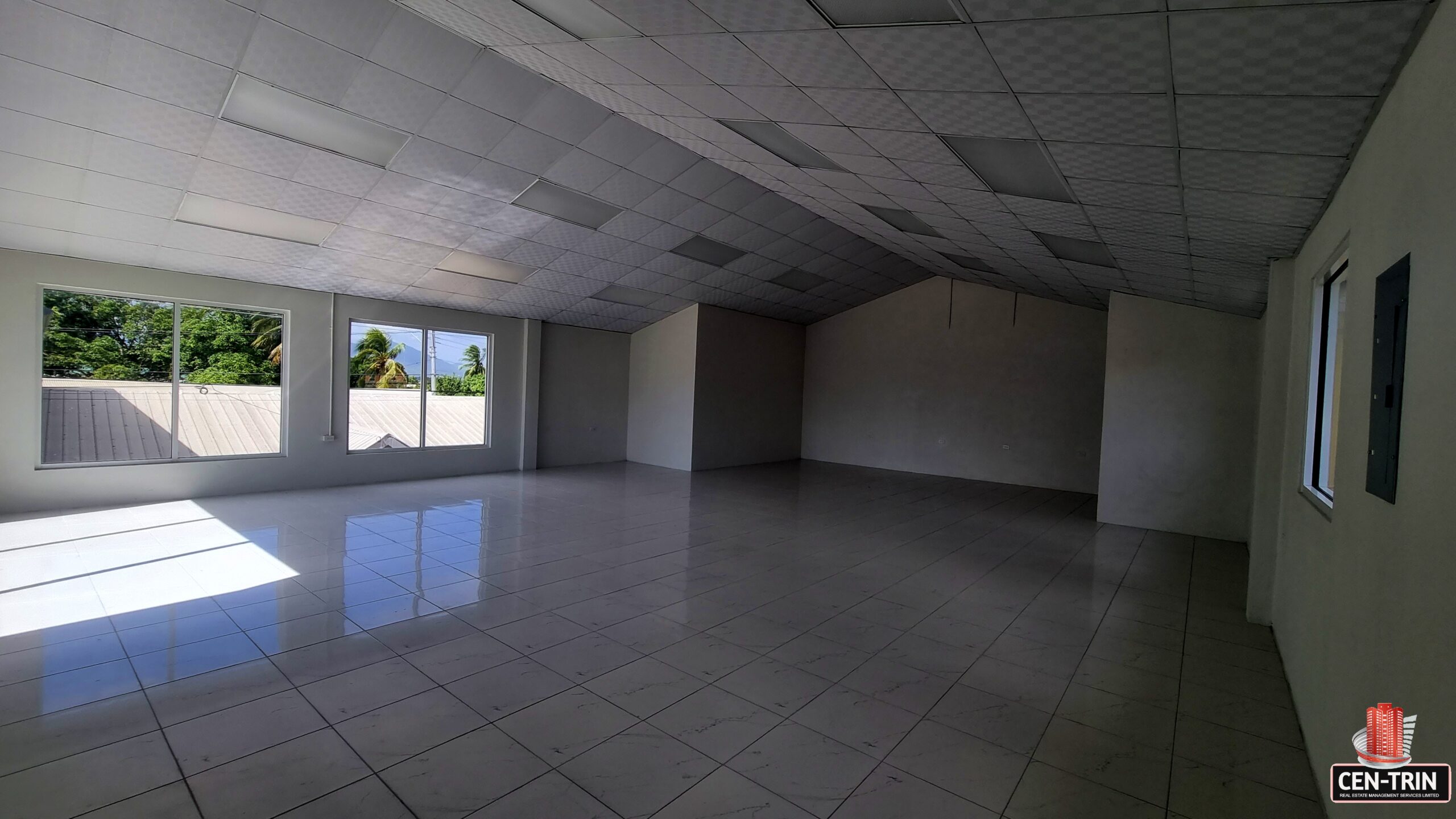 A large, empty room with expansive windows along one wall. Sunlight streams through the windows, illuminating the dust particles floating in the air.
