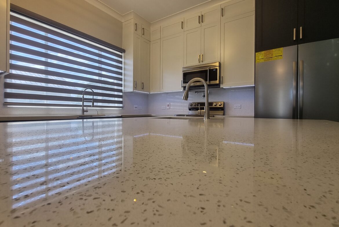 Modern kitchen with mobile kitchen island featuring microwave and stove, with refrigerator in the background in a Freeport home.