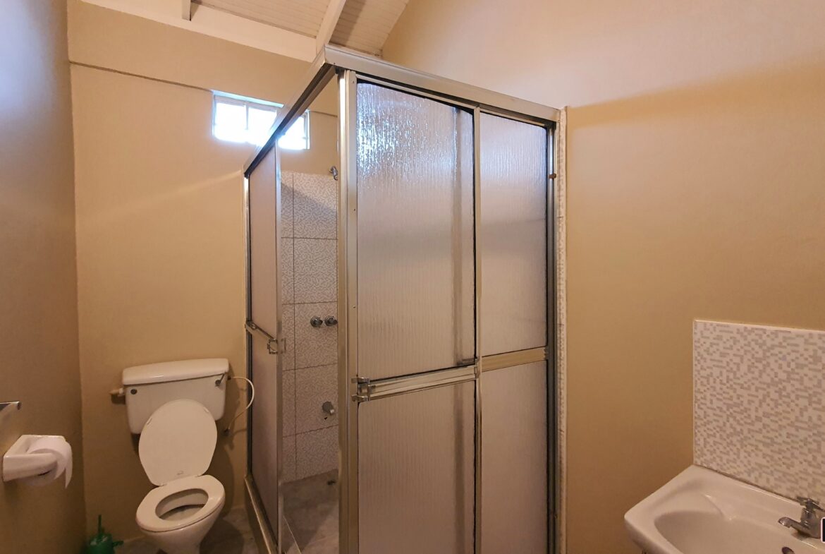 A charming bathroom with a toilet, shower with a glass door, and a sink with a mirror.