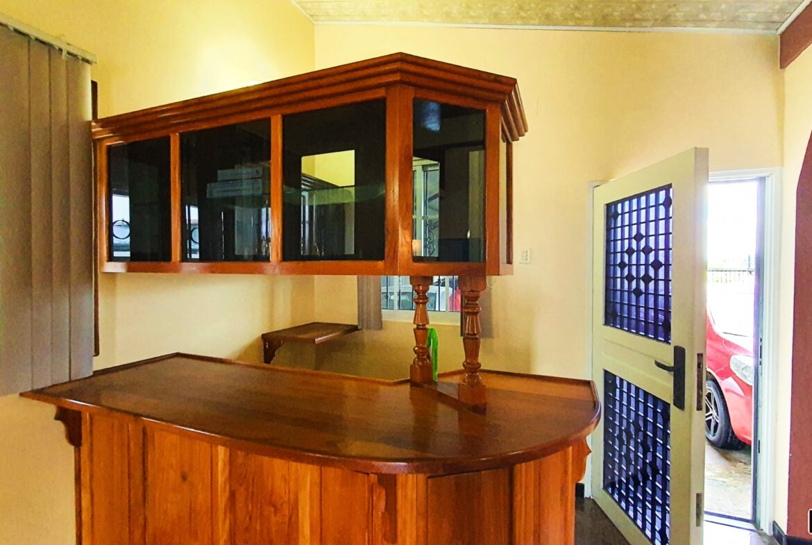 A charming kitchen with a bar area, cabinets, and a view of a red car parked outside through an open door.