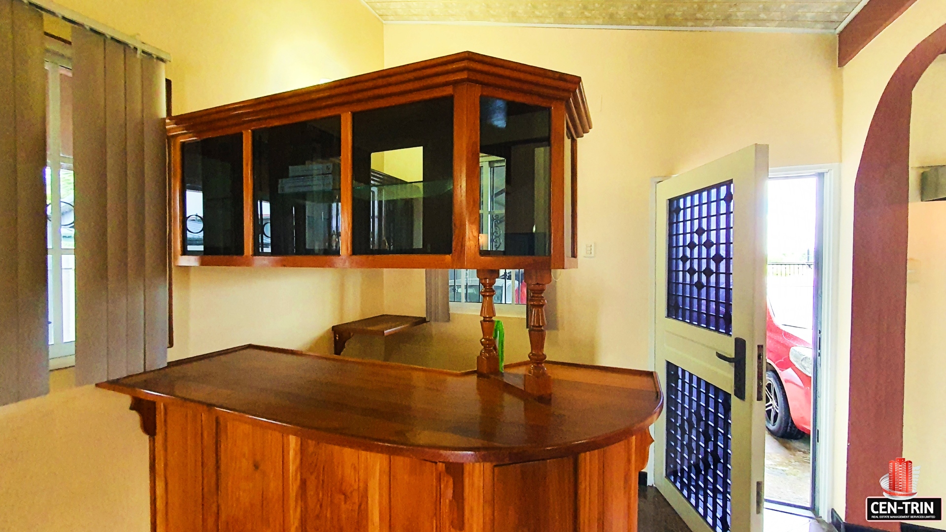 A charming kitchen with a bar area, cabinets, and a view of a red car parked outside through an open door.