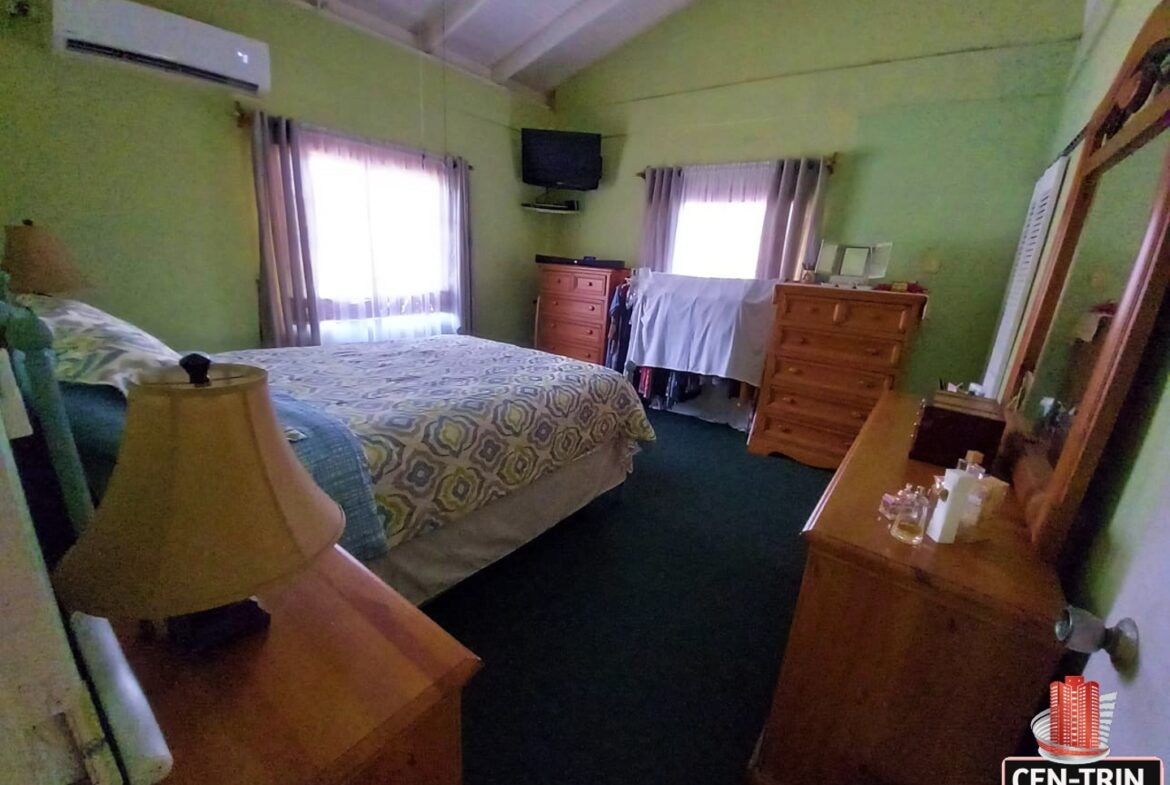 A bedroom with a wooden bed frame, dresser with mirror, and a flat screen television mounted on the wall.