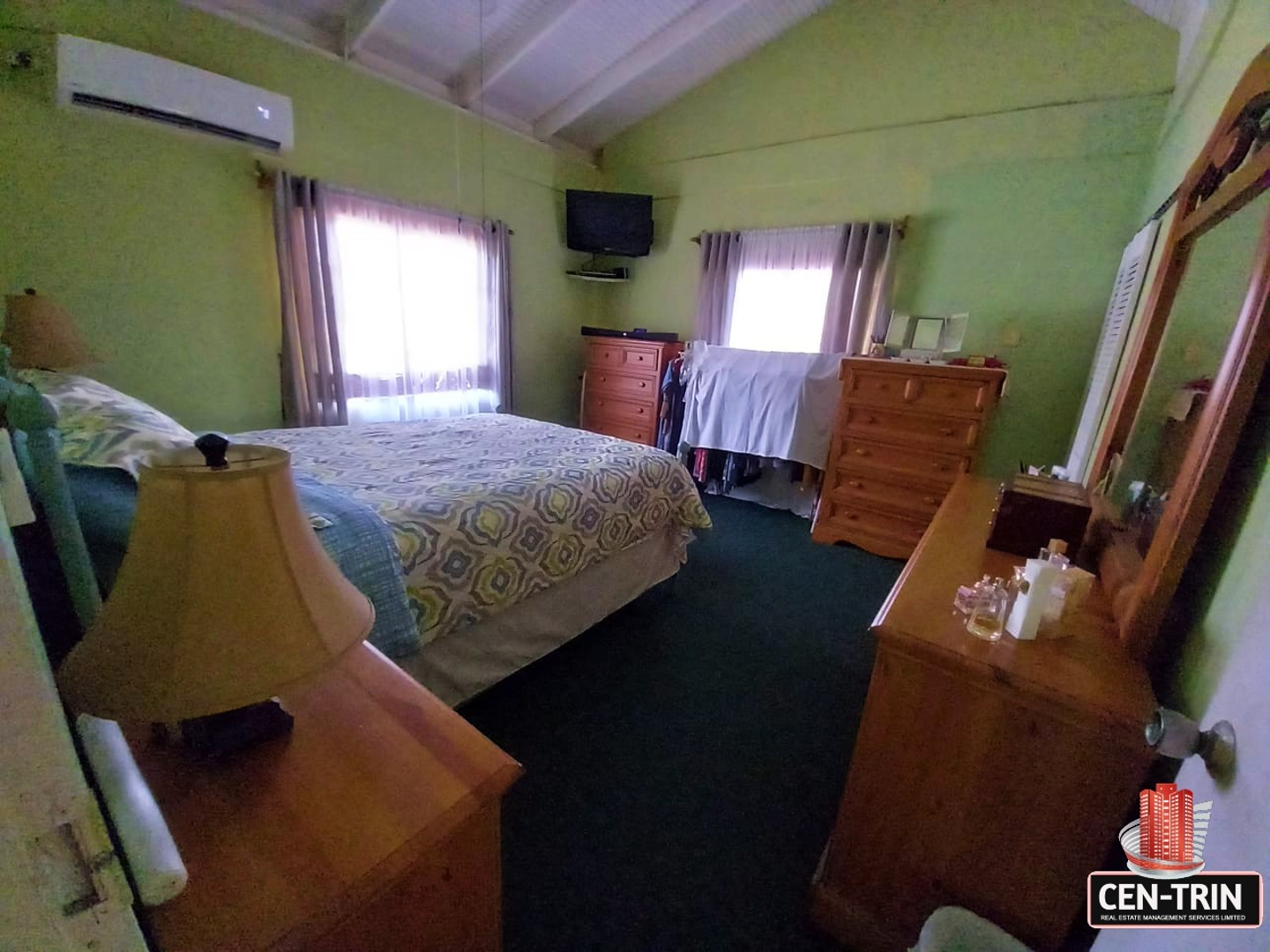 A bedroom with a wooden bed frame, dresser with mirror, and a flat screen television mounted on the wall.