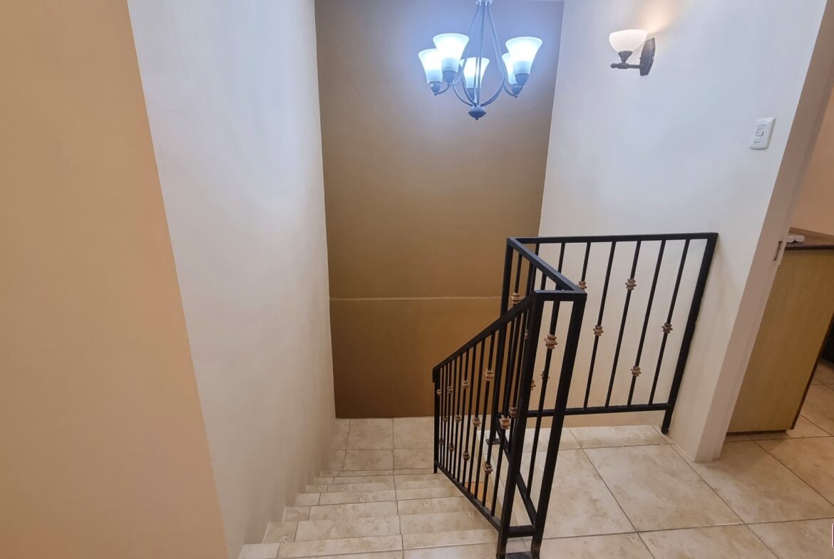 Staircase with wrought iron railing and chandelier in townhouse for sale.