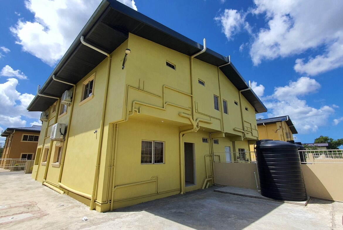 Exterior of a yellow townhouse with a black water tank.