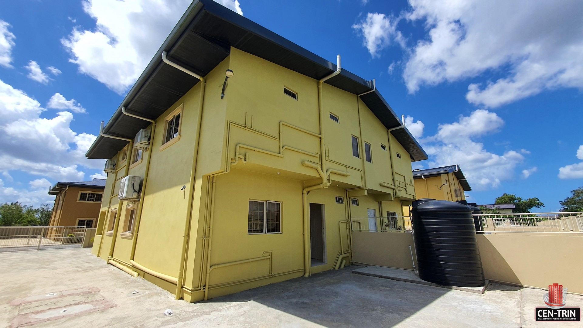 Exterior of a yellow townhouse with a black water tank.