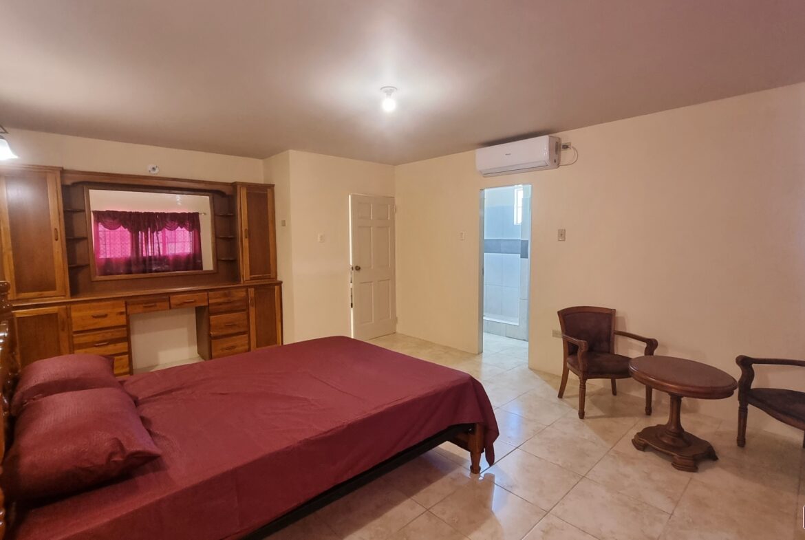Master bedroom in townhouse for sale with a king-size bed, two bedside tables with lamps, a dresser with mirror, and a window.