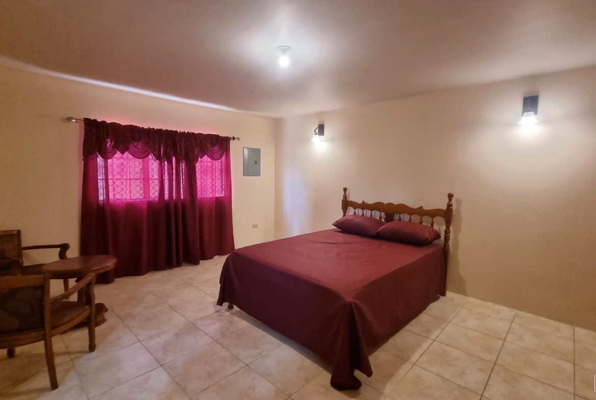 Master bedroom in townhouse for sale with a king-size bed, dresser, mirror, two windows, and a carpeted floor.
