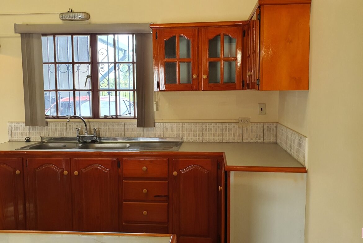 A charming kitchen with a farmhouse sink, white cabinets, and a window with a plant on the sill.