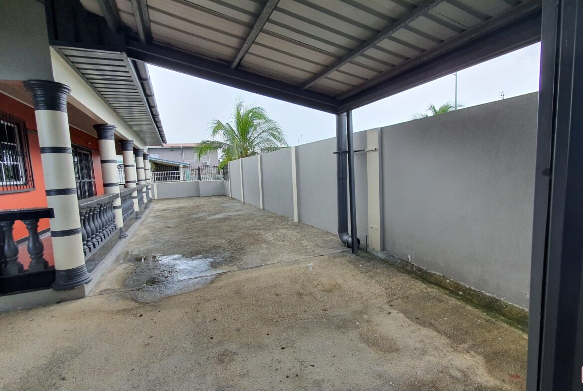 A house exterior with a covered driveway and a wall.