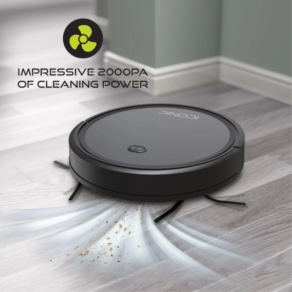 A black robot vacuum cleaner, the Tzumi SmartClean 2000, cleaning a hardwood floor and picking up dust and debris.
