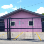 Front view of a pink one-story apartment for rent Jerningham with a black metal security gate and a paved parking area of this lovely apartment for rent