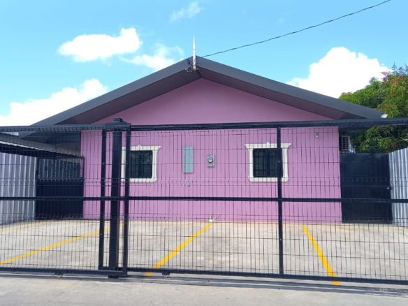 Front view of a pink one-story apartment for rent Jerningham with a black metal security gate and a paved parking area of this lovely apartment for rent