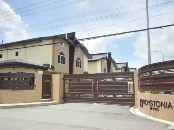 Roystonia Mews Townhouse for Sale Piarco, Trinidad | $1.99M 10 Exterior view of Roystonia Mews showing the gated entrance with a sign, townhouses, and overhead power lines.