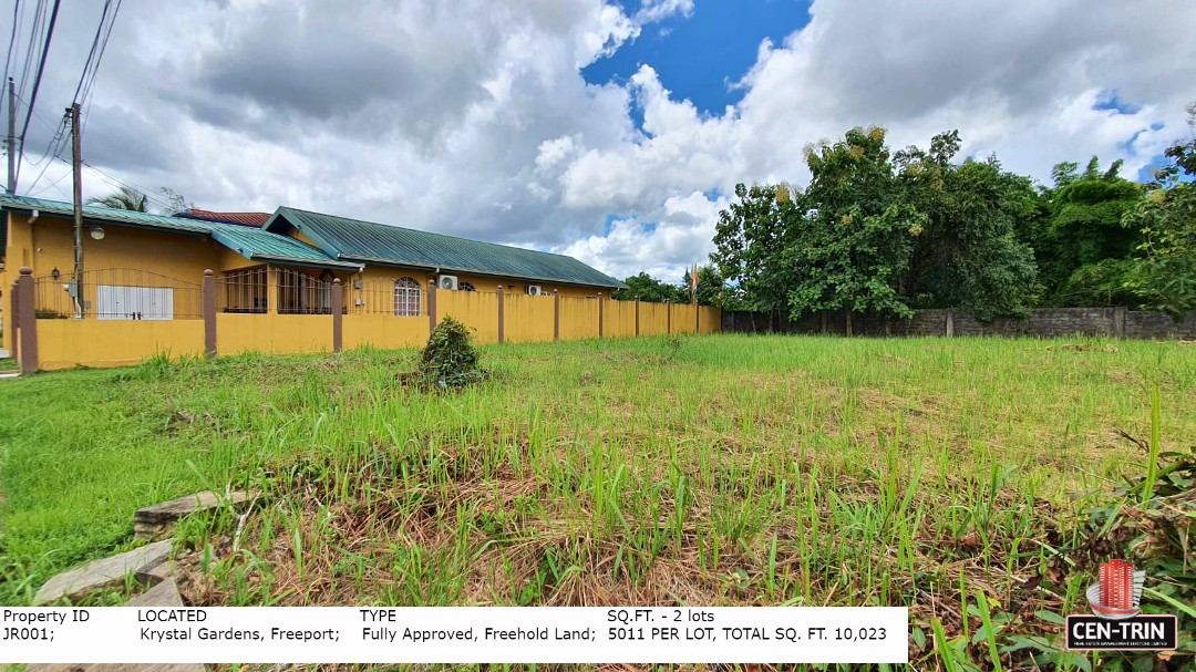 A view of the vacant, grassy land for sale in Trinidad, showing a residential building next door and emphasizing the clear space available for development in Krystal Gardens, Freeport.