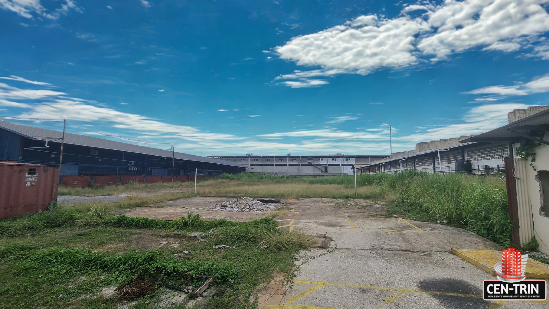 Ground-level view of the commercial land for rent on Patraj Trace, Aranguez, showing a cleared portion in the foreground, with existing commercial buildings in the background under a blue sky.