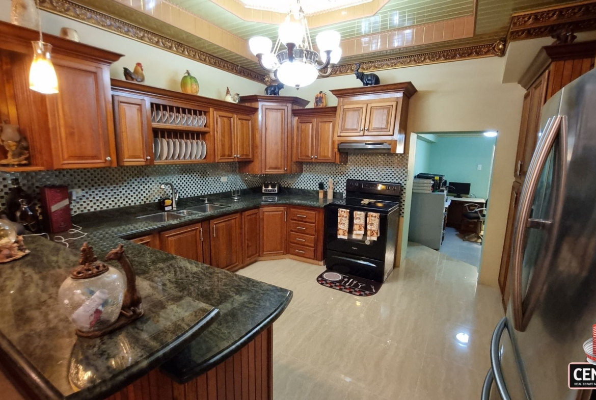 Spacious internal kitchen with elegant wooden cabinetry, granite countertops, and modern appliances in this luxury home for sale in Cunupia