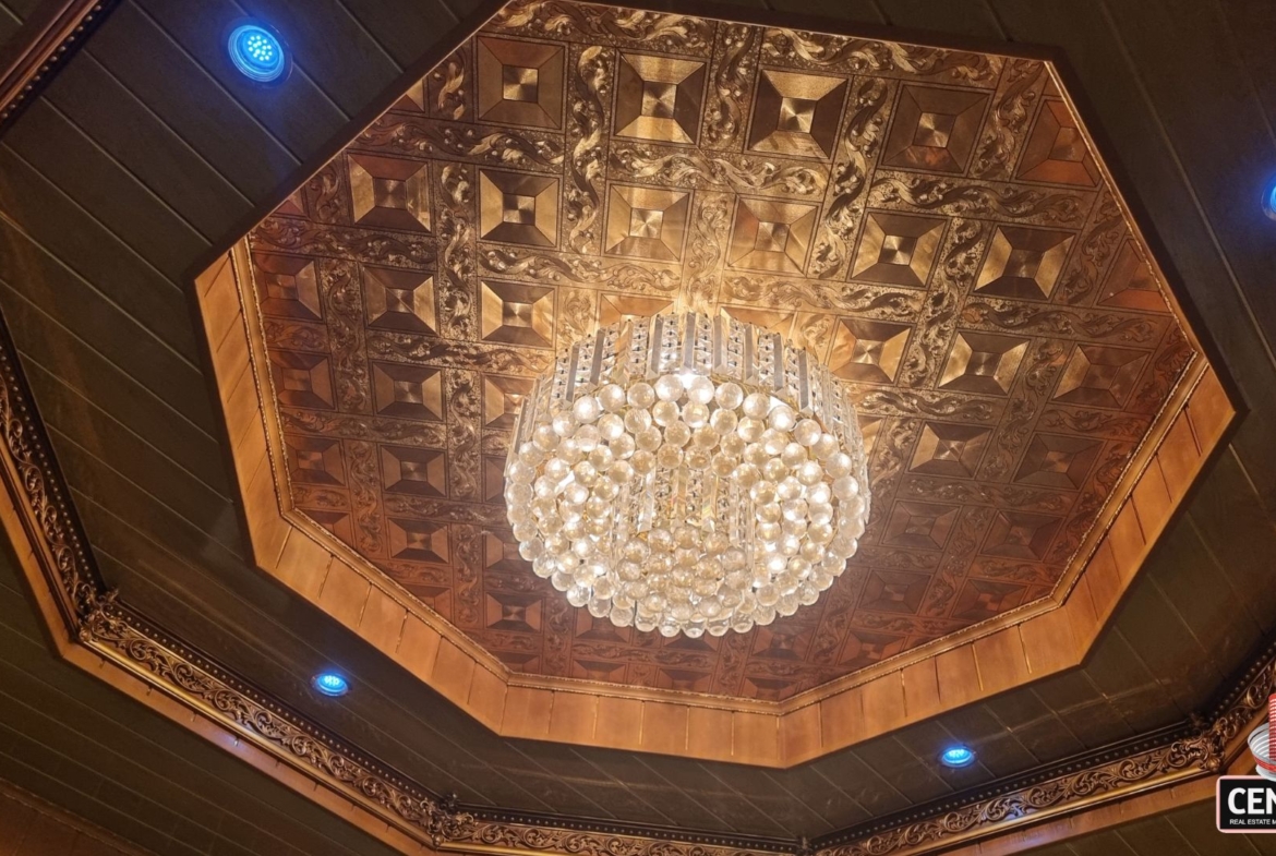 Ornate, decorative ceiling with a large crystal chandelier and recessed blue lighting in this luxury home for sale in Cunupia