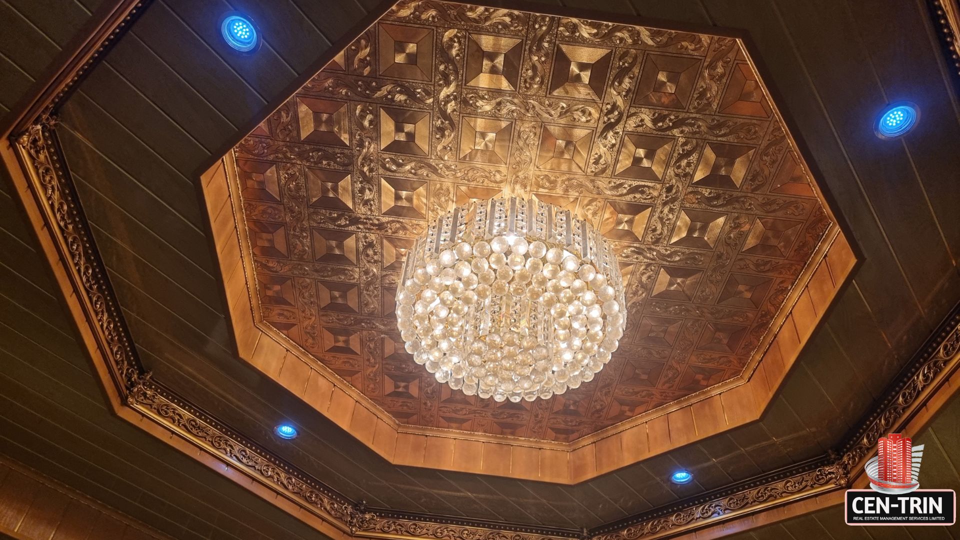 Ornate, decorative ceiling with a large crystal chandelier and recessed blue lighting in this luxury home for sale in Cunupia