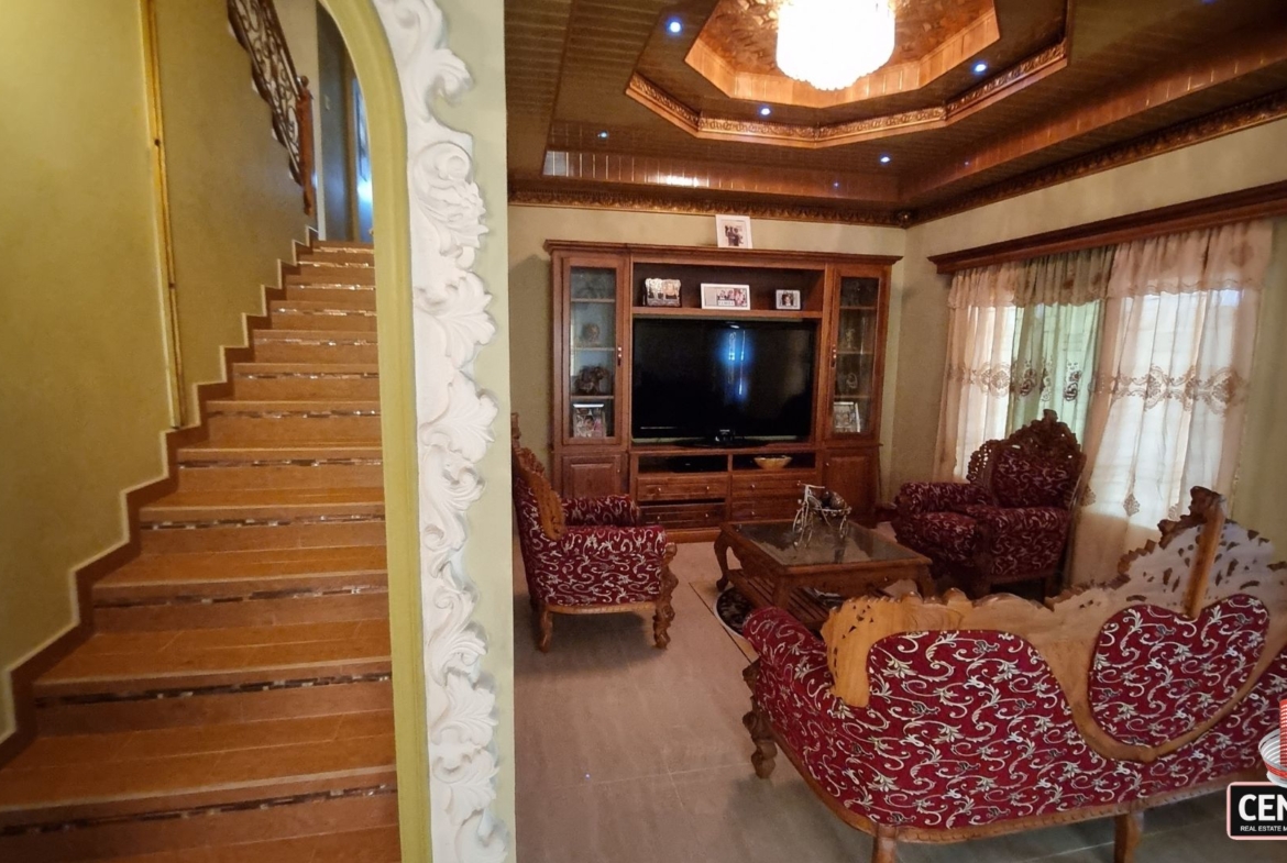 View of the grand staircase adjacent to the furnished living area in this luxury home for sale in Cunupia