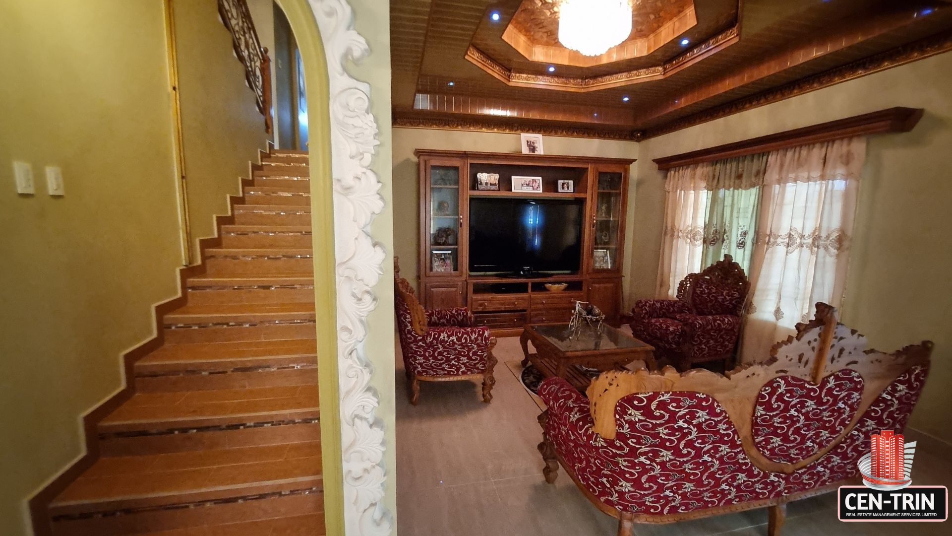View of the grand staircase adjacent to the furnished living area in this luxury home for sale in Cunupia