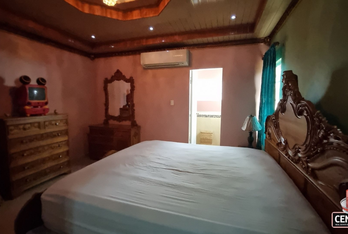 Beautifully furnished bedroom with carved wooden bed, dresser, and private en-suite bath in this luxury home for sale in Cunupia