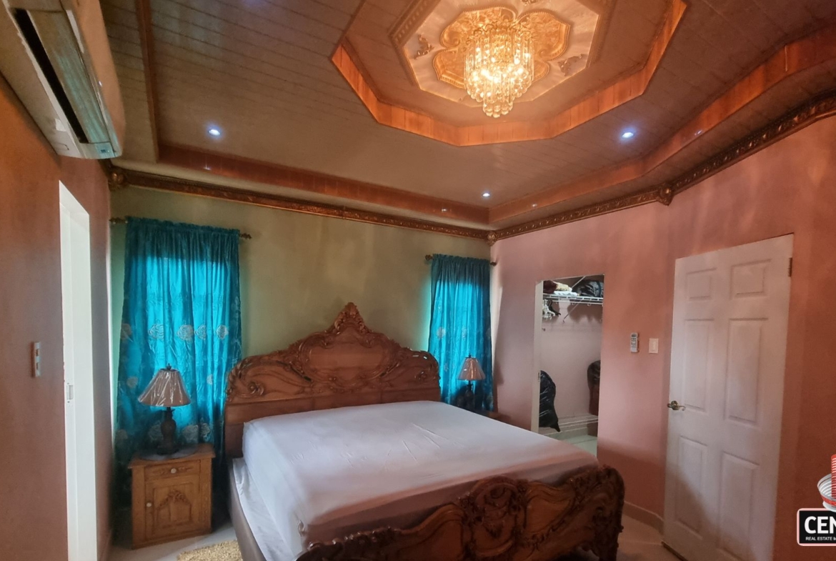 Luxurious bedroom with carved bed, air conditioning, and access to a walk-in closet in this luxury home for sale in Cunupia