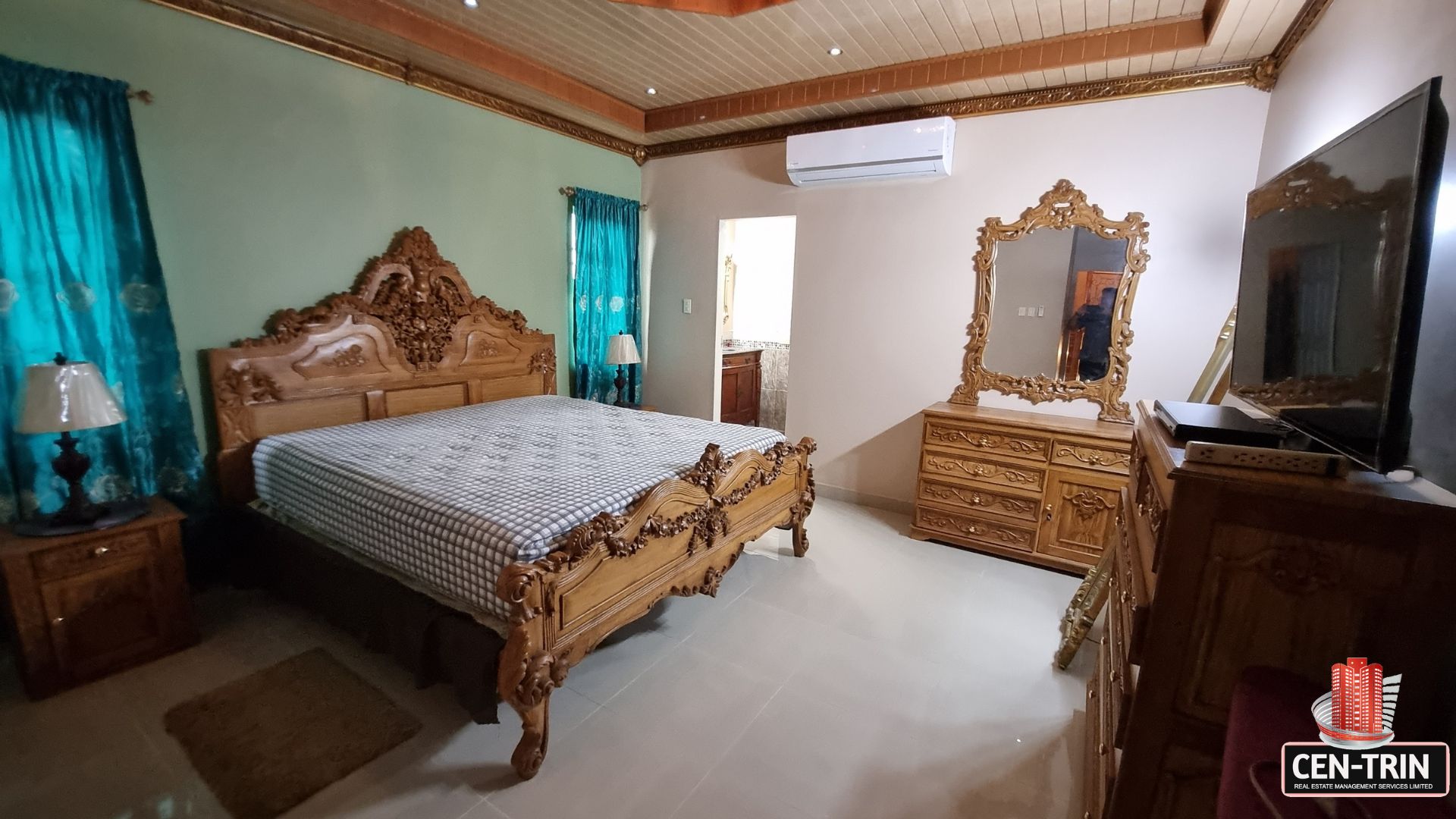 Full view of the beautifully furnished bedroom with carved wooden bed, dresser, air conditioning, and direct en-suite access in this luxury home for sale in Cunupia.