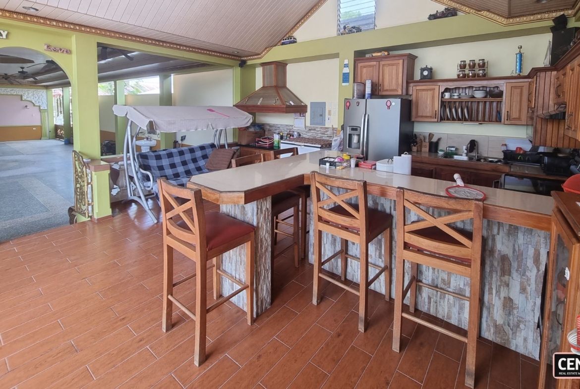 Spacious external living area with kitchen island and high ceilings in this luxury home for sale in Cunupia