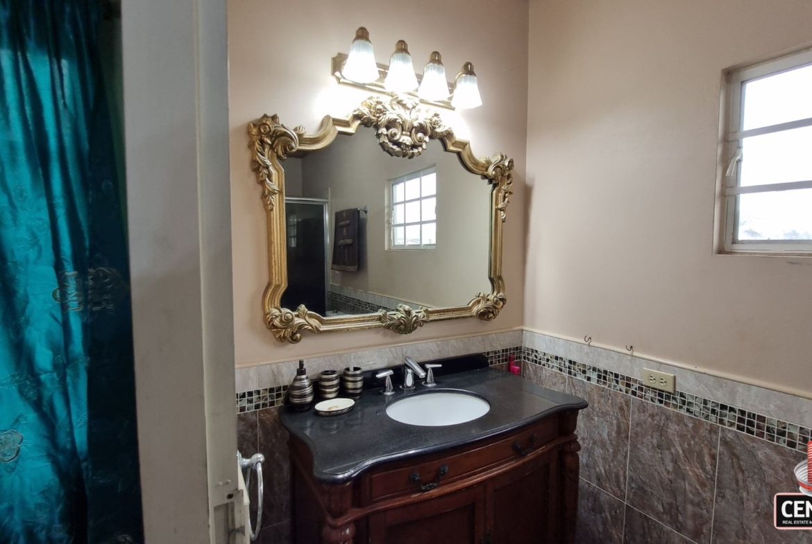 Elegant en-suite bathroom vanity with ornate mirror, sophisticated lighting, and dark countertops in this luxury home for sale in Cunupia