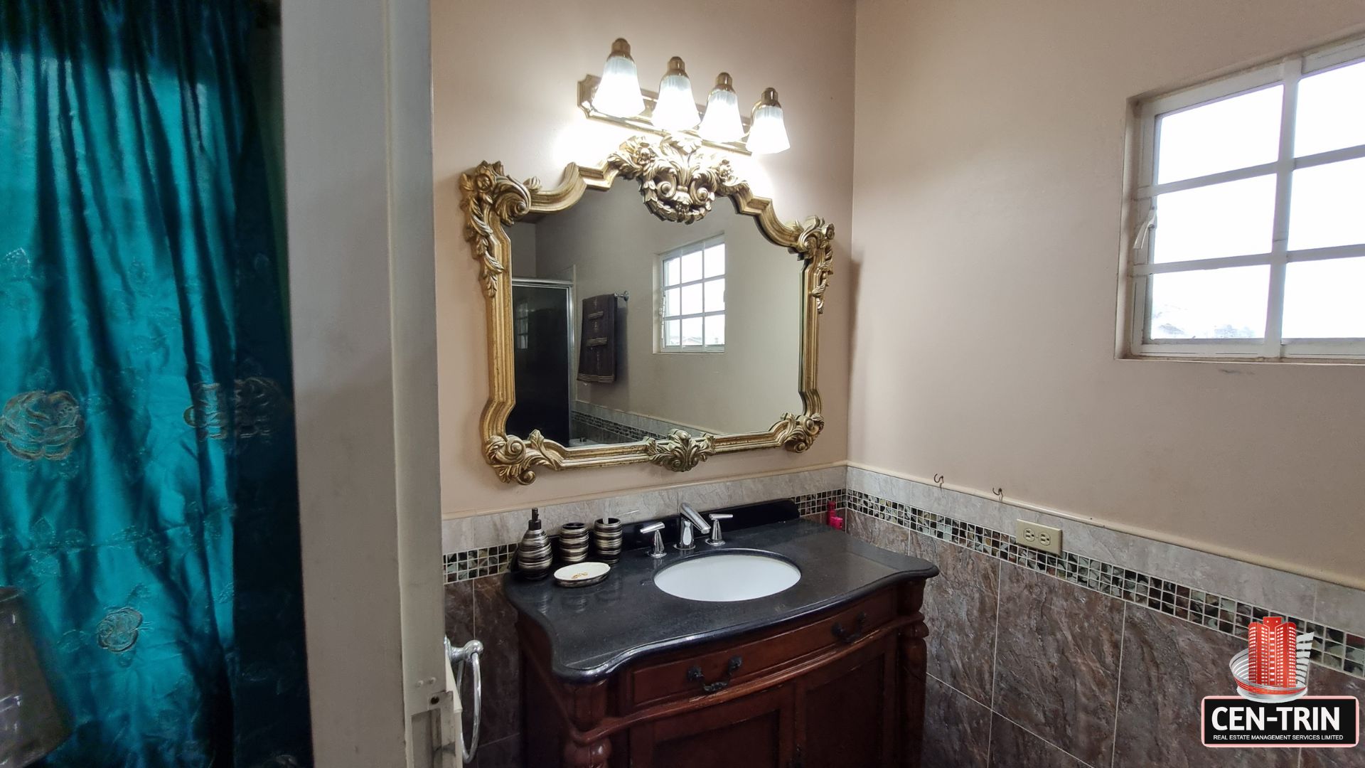 Elegant en-suite bathroom vanity with ornate mirror, sophisticated lighting, and dark countertops in this luxury home for sale in Cunupia