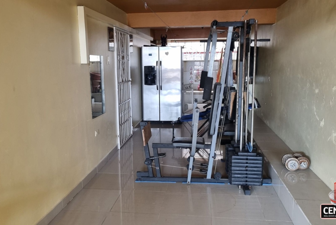 Dedicated gym space with exercise equipment and a large refrigerator in this luxury home for sale in Cunupia