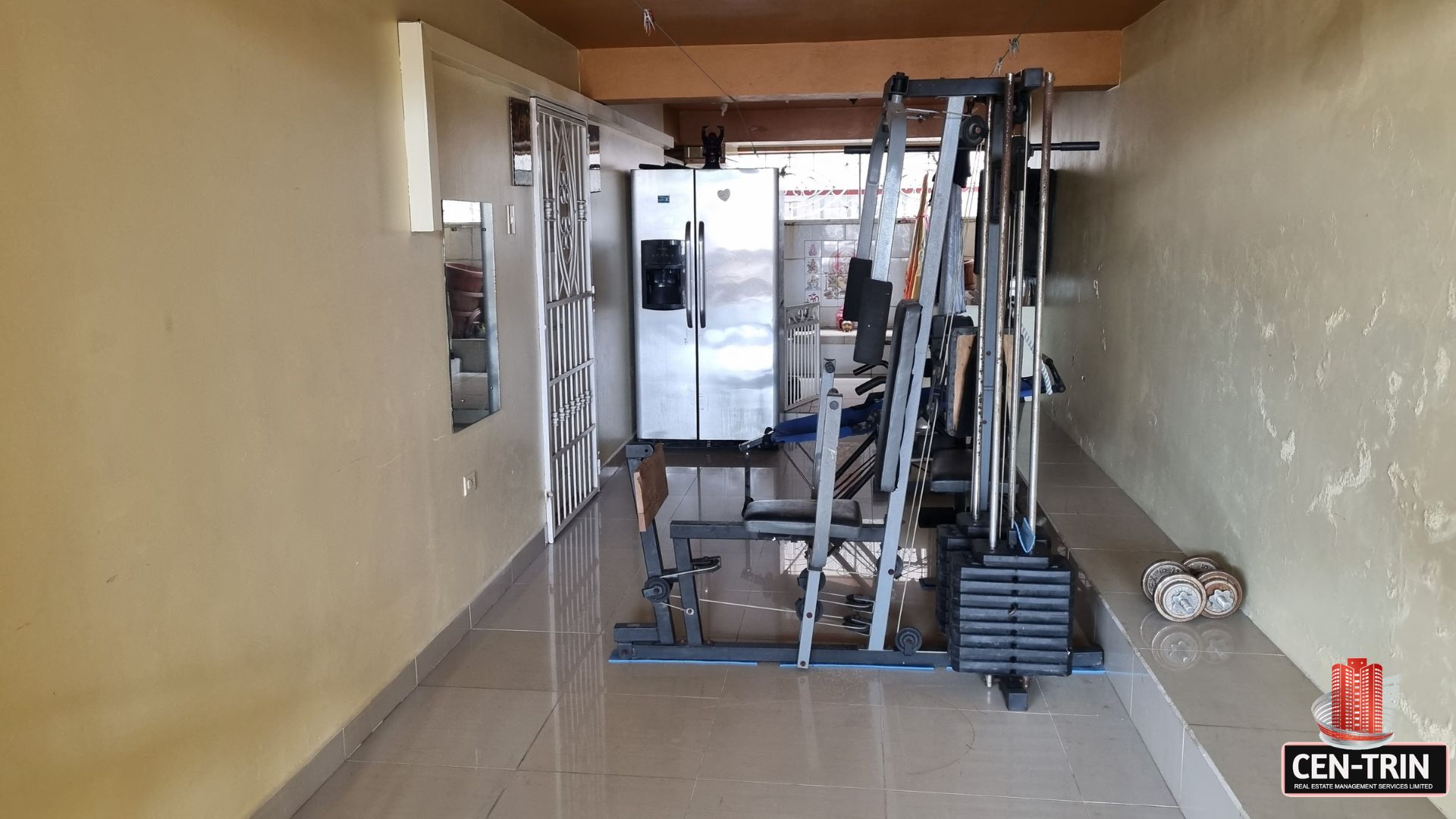 Dedicated gym space with exercise equipment and a large refrigerator in this luxury home for sale in Cunupia