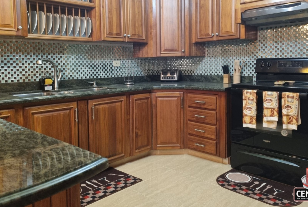 Well-appointed internal kitchen with wooden cabinets and mosaic tile backsplash in this luxury home for sale in Cunupia
