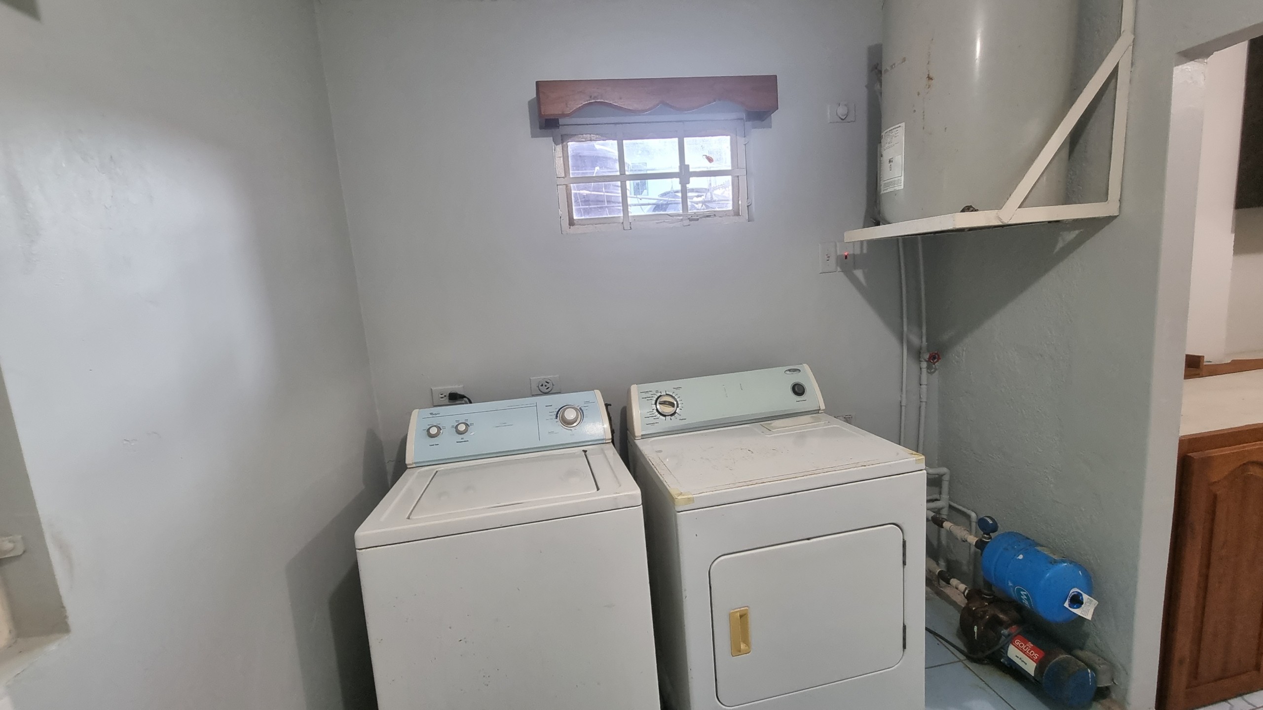 Equipped Laundry Area with Water System in Fully Furnished House for Sale Laundry area in a fully furnished house for sale, showing a washing machine, dryer, water heater, and water pump system.