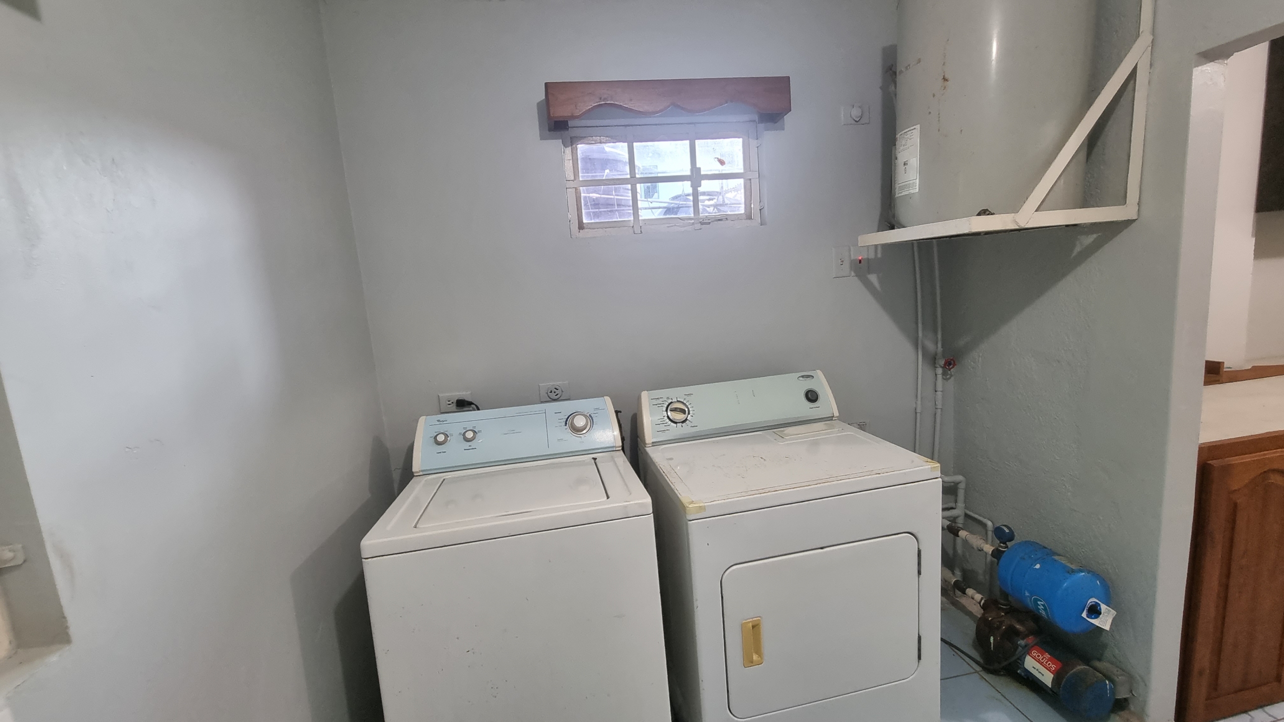 Laundry area in a fully furnished house for sale, showing a washing machine, dryer, water heater, and water pump system.