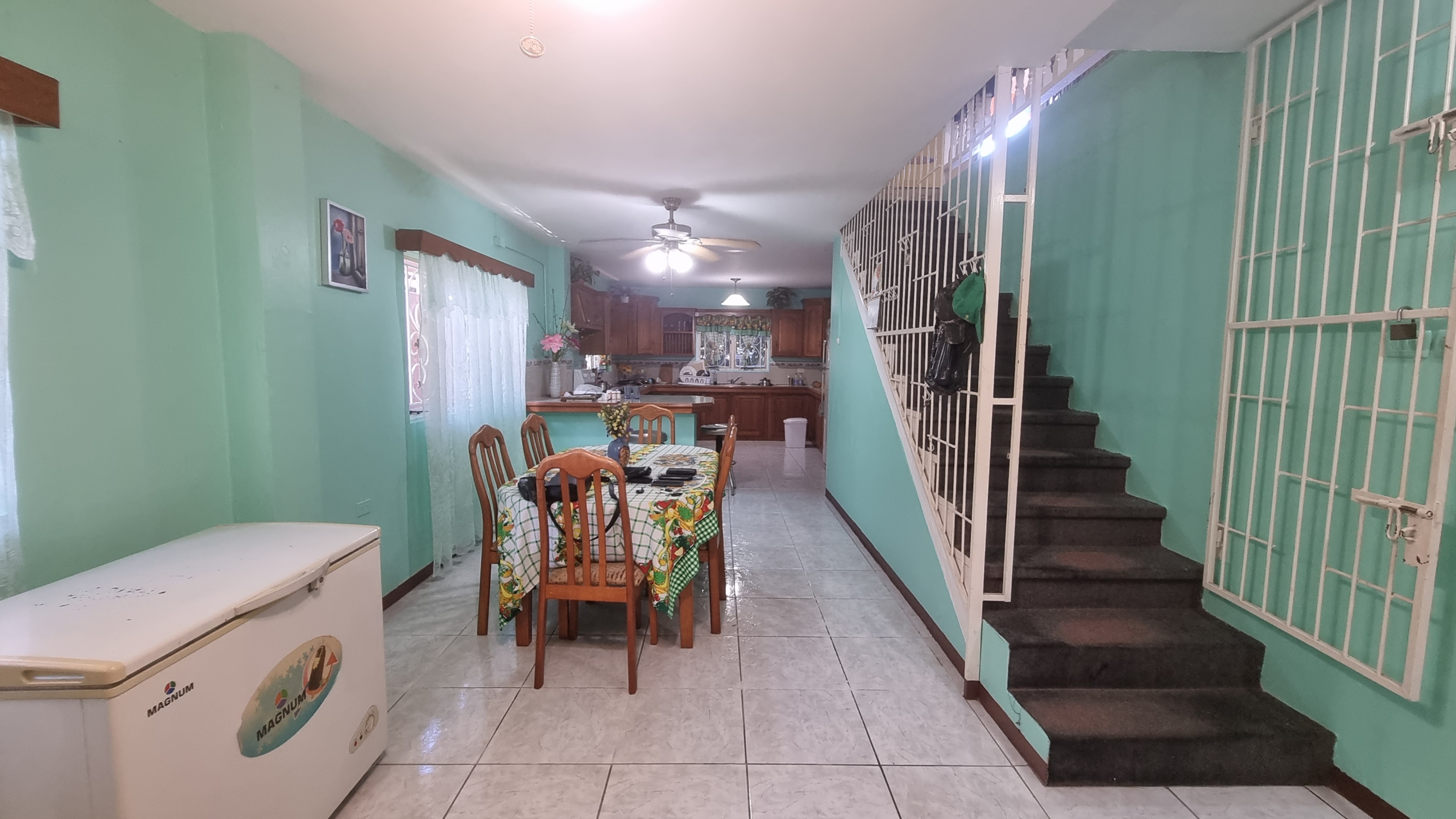 Open-plan dining and kitchen area with a chest freezer, dining table, and staircase leading upstairs, in a fully furnished house for sale.