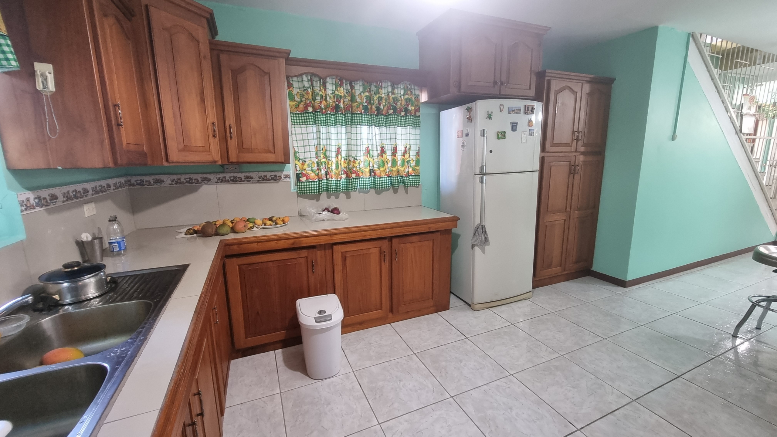 Kitchen view showing ample wooden cabinets, a white refrigerator, and a double sink, in a fully furnished house for sale.