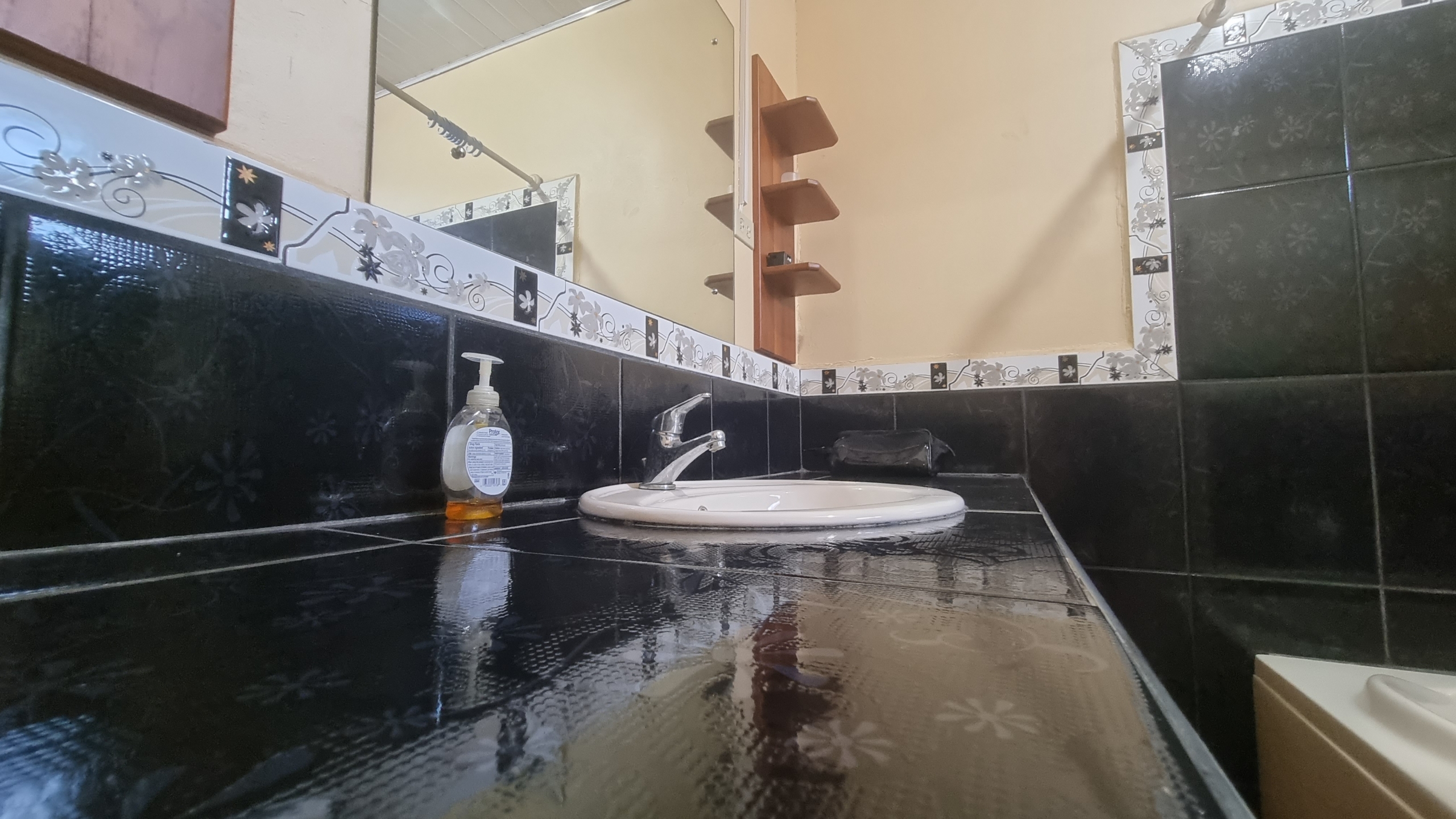 Bathroom vanity with a white basin sink, modern faucet, dark tiled countertop and walls, and a large mirror in a fully furnished house for sale.