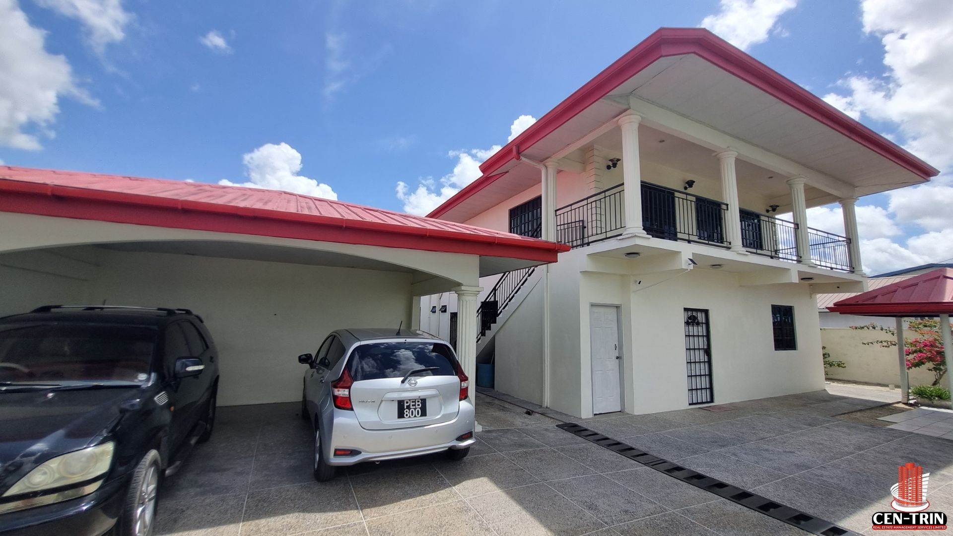 Front view of a two-story apartment building for sale in Chaguanas, featuring a red roof, white exterior, covered parking for two vehicles, and an inviting entrance, ideal for a rental investment.