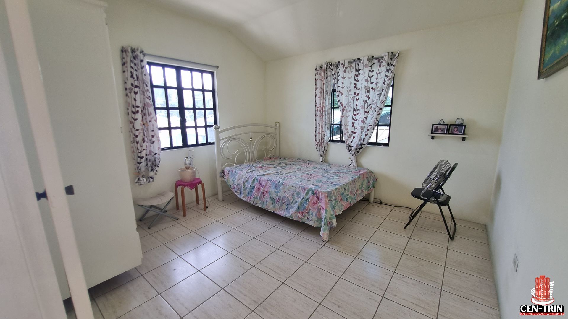 Another spacious bedroom in this Home For Sale in Trinidad, with a decorative bed frame, two windows with curtains, and tiled flooring, suitable for semi furnished setups and a strong rental investment.