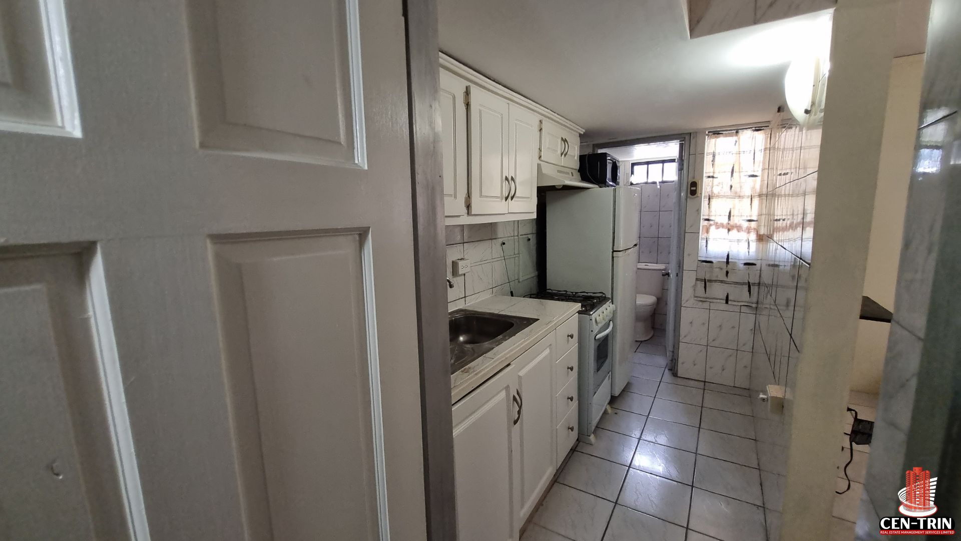 Compact kitchen area in a Home For Sale in Trinidad, featuring white cabinets, sink, stove, and refrigerator, showing semi furnished potential within a rental investment unit.