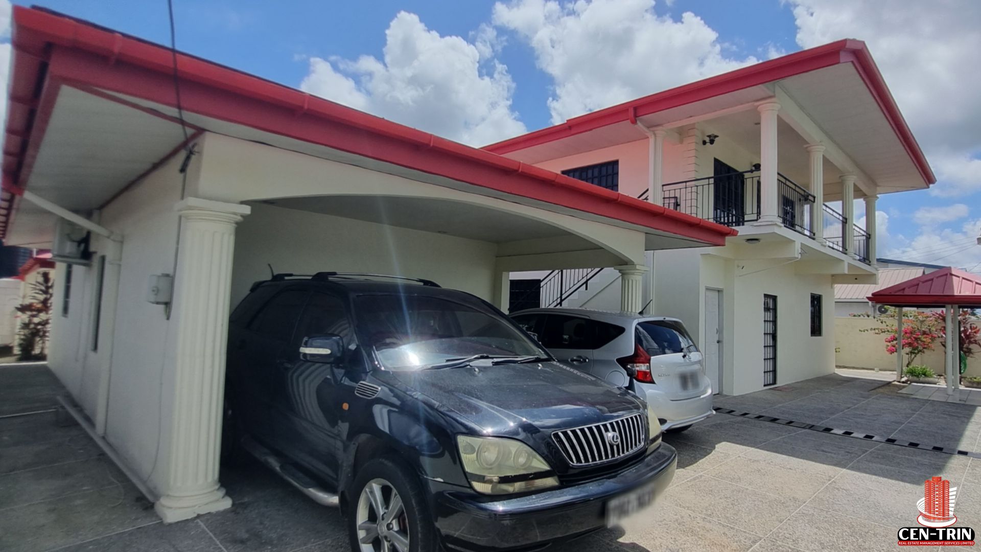Exterior view of a Home For Sale in Trinidad, showcasing the covered parking area for multiple vehicles, red roof, and white facade, highlighting its potential as a rental investment.