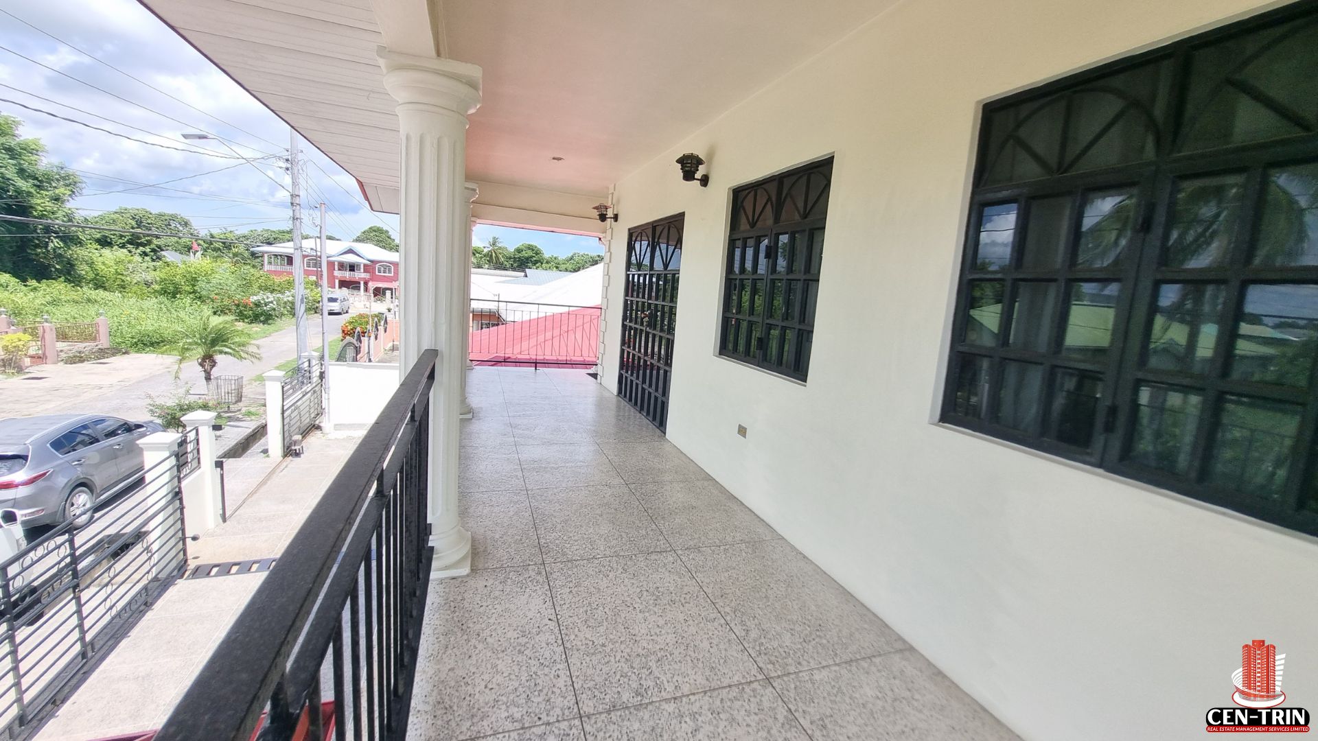 View from the upper-level balcony of a multi-unit apartment building for sale in Chaguanas, featuring white pillars, black railings, and multiple entrances, highlighting potential semi furnished living spaces for rental investment.