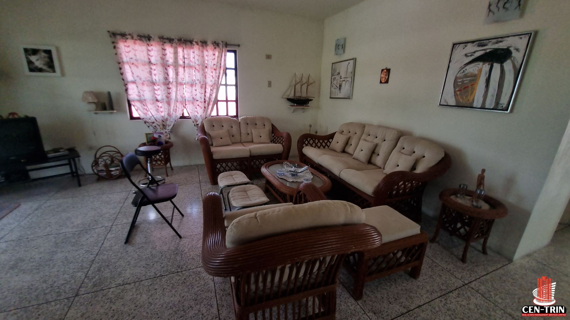 Interior living room of an apartment building for sale in Chaguanas, featuring semi furnished rattan furniture, tiled floors, and decorative items, showcasing a comfortable space for a rental investment.