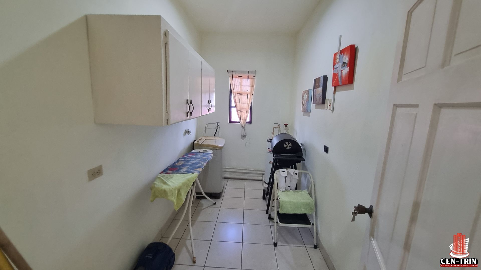 Utility room in a Home For Sale in Trinidad, featuring an ironing board, washing machine, and cabinets, useful for semi furnished units and enhancing rental investment appeal.