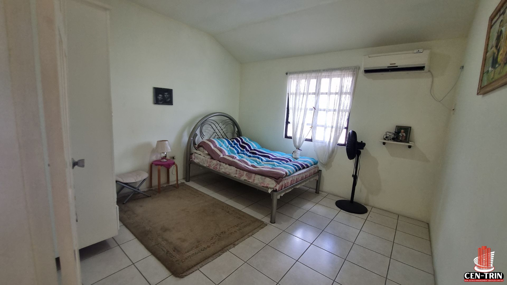A comfortable bedroom in this Home For Sale in Trinidad, featuring a bed, air conditioning unit, and tiled floor, suitable for semi furnished living and contributing to a strong rental investment.