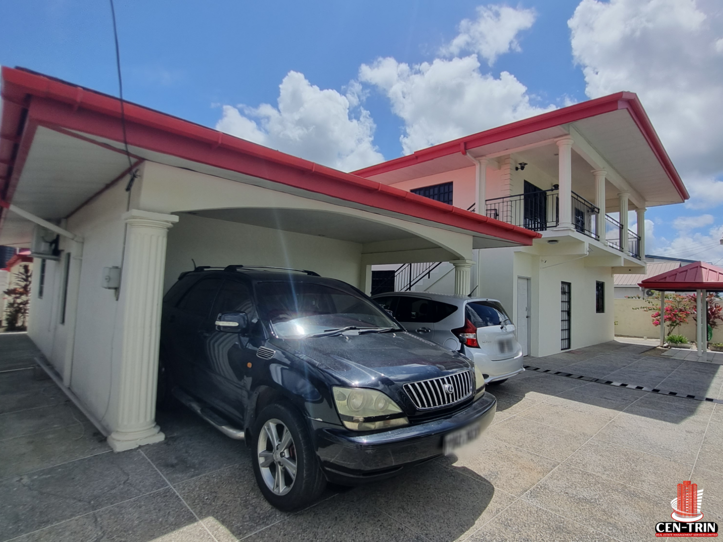 Front view of a modern two-story Home For Sale in Trinidad, with a red roof, white exterior, covered carport for two vehicles, and an open paved driveway.