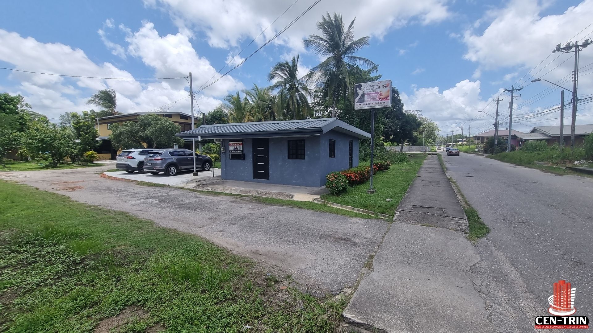 A wider view of the gray commercial rental building and its designated parking area on Chin Chin Road, with a neighboring salon's sign in the background.